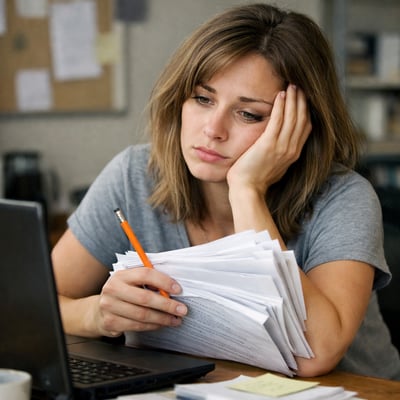 a woman in front of her computer holding a pencil and a stack of papers looking tired-1