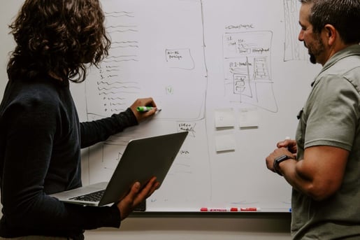 msp managed service provider writing gameplan on whiteboard holding laptop explaining to man