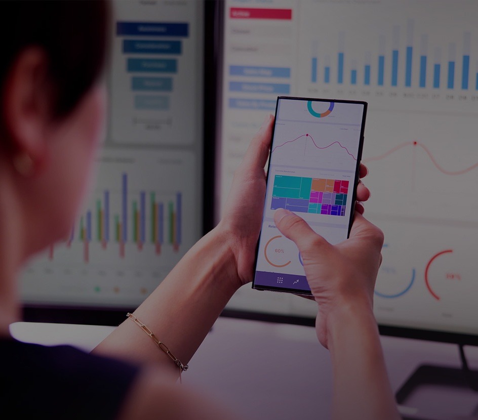personalized banking woman holding cell phone looking at bank account computer in background with graphs