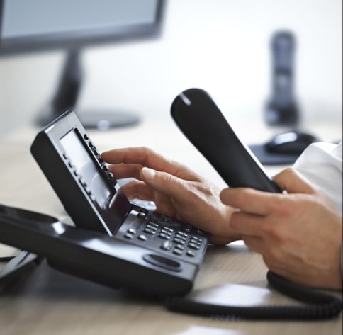 voip phone system mans hand picking up phone on desk